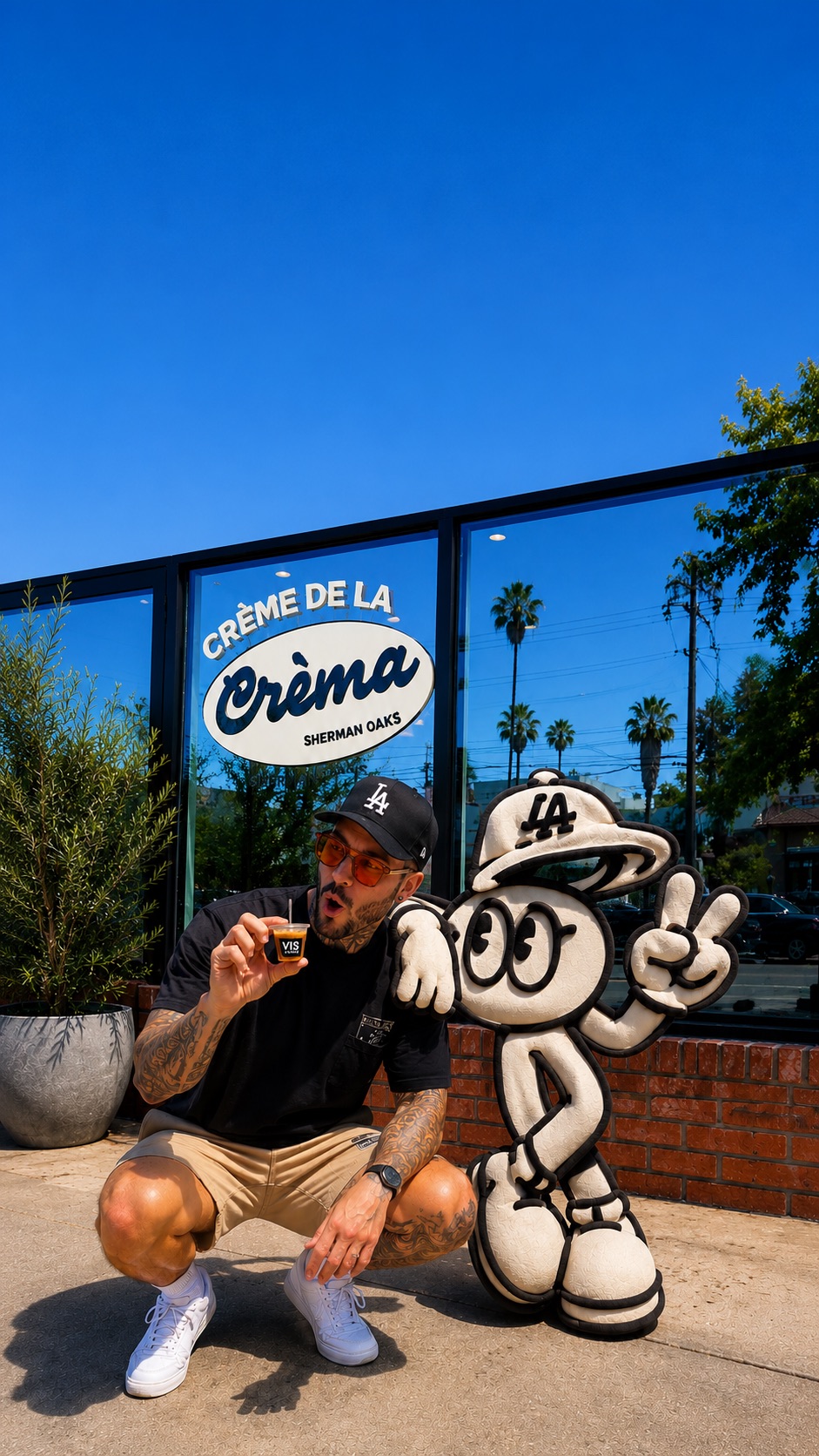 Kyle holding a small coffee beside a playful coffee cup character outside Crema in Sherman Oaks