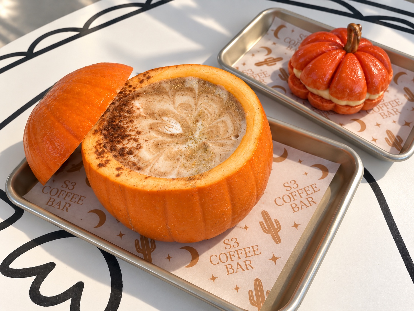A PSL served inside a real pumpkin beside a pumpkin shaped bagel with cream cheese on S3 trays