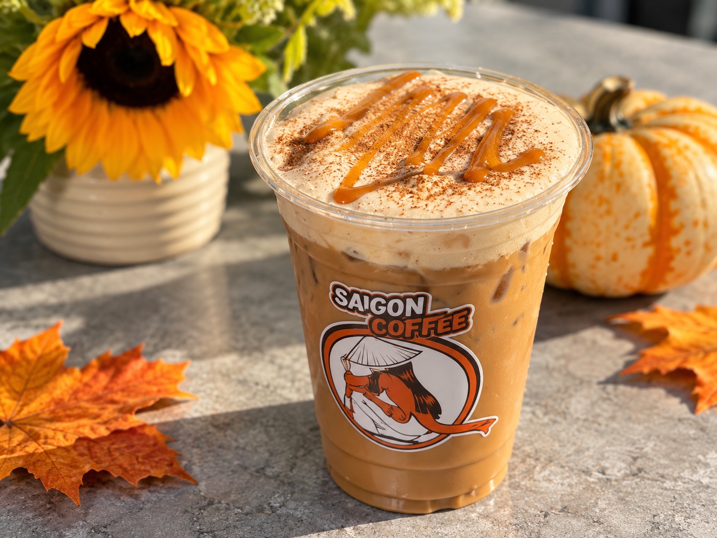 An iced Saigon Coffee drink surrounded by autumn leaves, a sunflower and a pumpkin